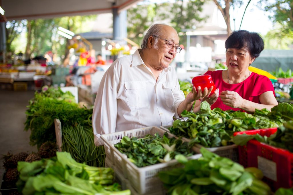 two older adults looking at vegetables at a farmers' market